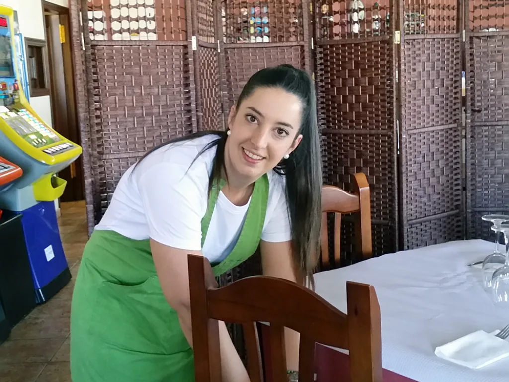 Eine junge Frau in Schürze deckt einen Tisch im Restaurant ein.